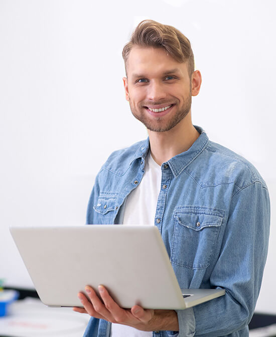 male-teacher-standing-holding-laptop-and-smiling-QRL8U3U